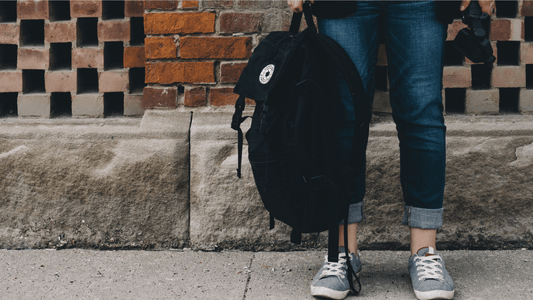 Image of student in jeans standing on concrete next to a red brick wall holding a black backpack ready to engage in mindful student planning.